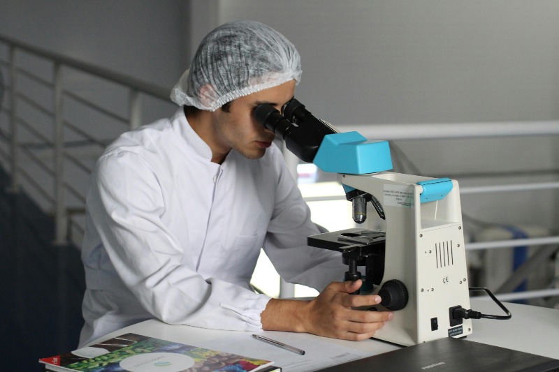 A researcher in a white lab coat focusing on a microscope in Fort Worth, TX
